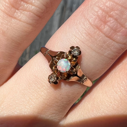Close-up of an antique opal and rose cut diamond ring worn on a finger in natural sunlight.  The round opal has pinkish red and green play of color.