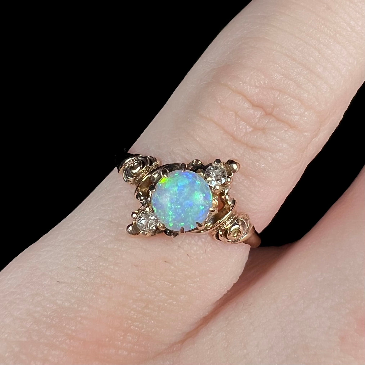 Close-up of antique three-stone pinky ring set with round Australian opal, flanked by two Old European Cut accent diamonds, worn on pinky finger