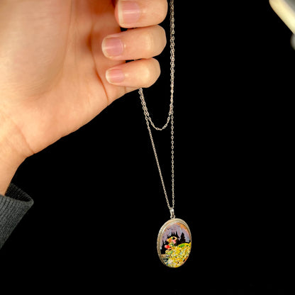A silver necklace with the image of a woman made from butterfly wing and crushed opal, held by a hand from its chain.
