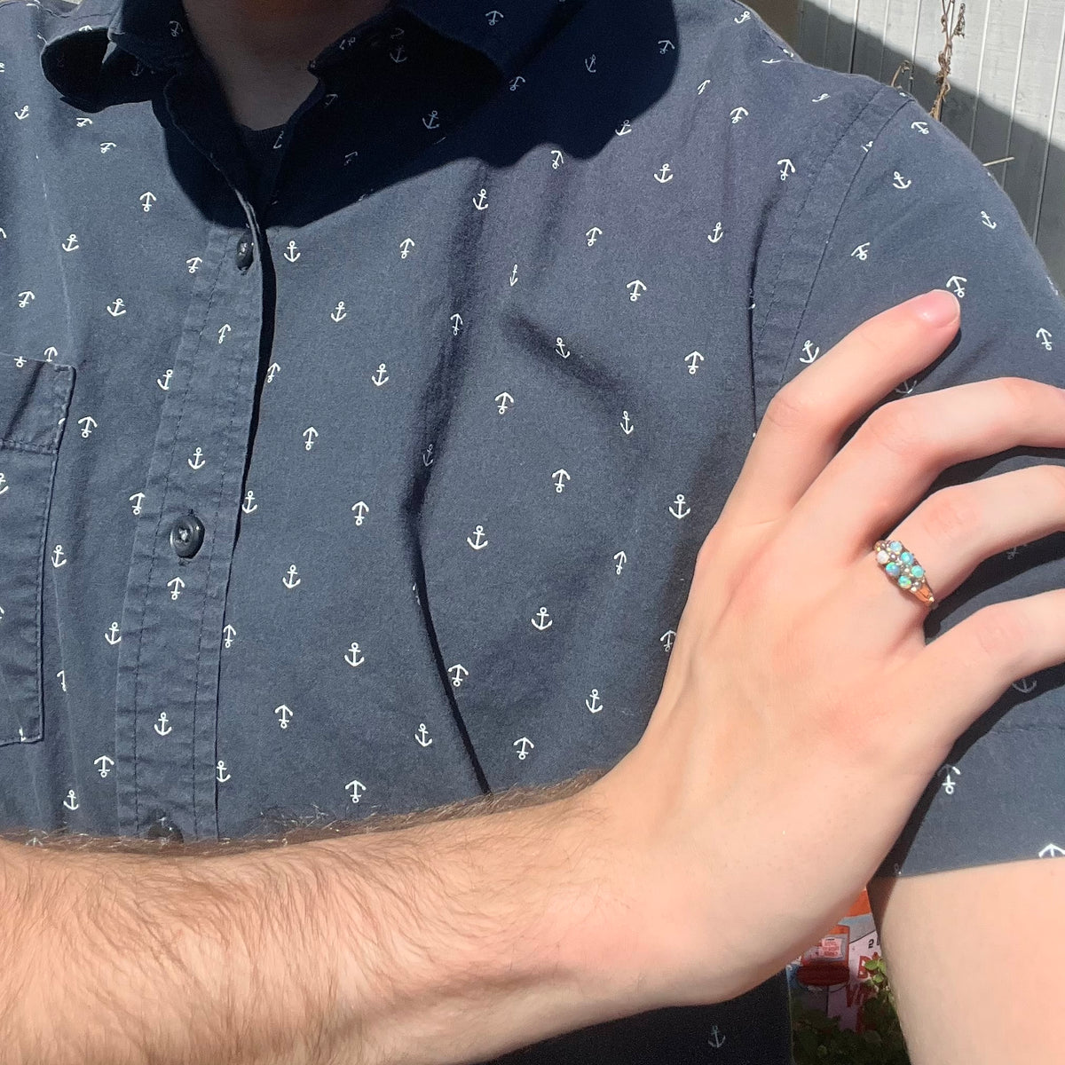 Close-up of person resting hand on opposing shoulder in sunlight wearing a women's antique six-stone opal ring with pearl accents in gold