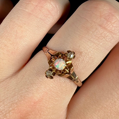 Close-up macro view of an antique three-stone opal and rose cut diamond ring worn on a finger under warm studio light.