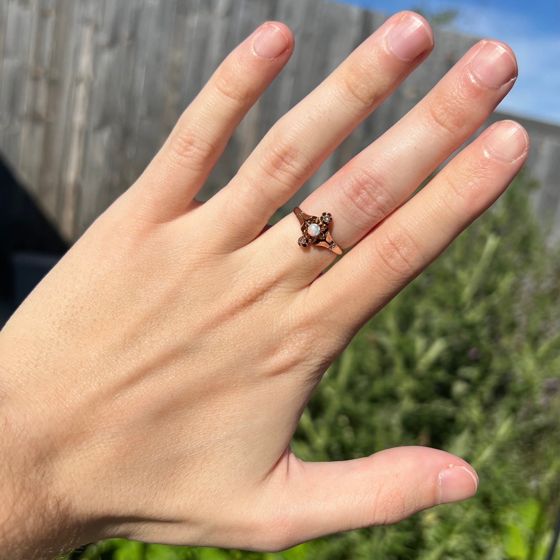 Hand wearing an antique Victorian opal and diamond ring in natural light against a blurry outdoor background.