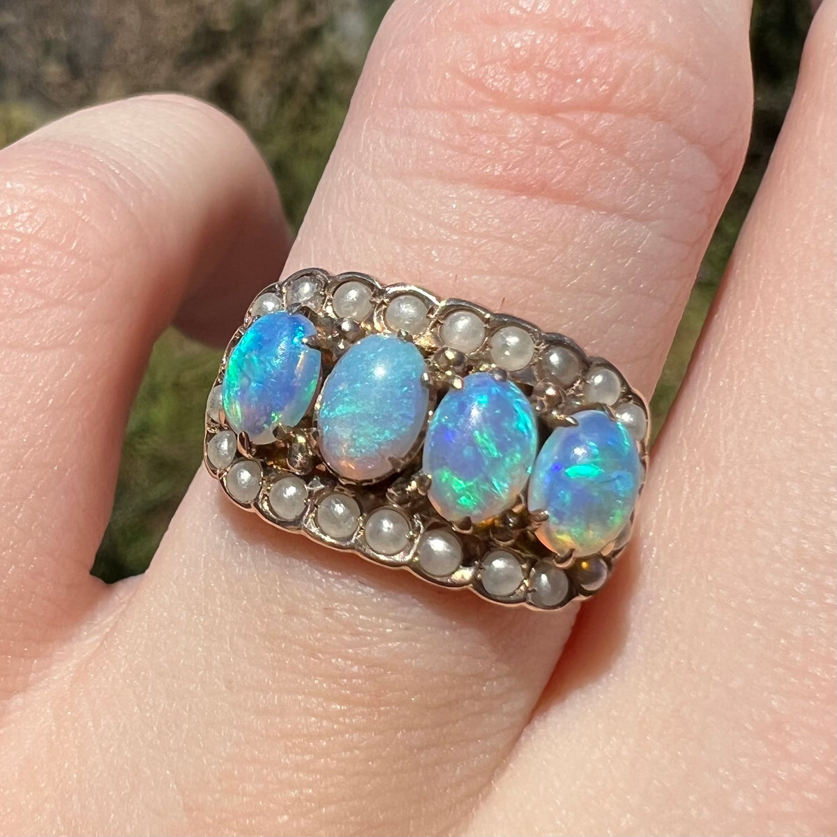 Macro close-up of antique Victorian crystal opal and seed pearl-accented ring, worn on finger in natural light