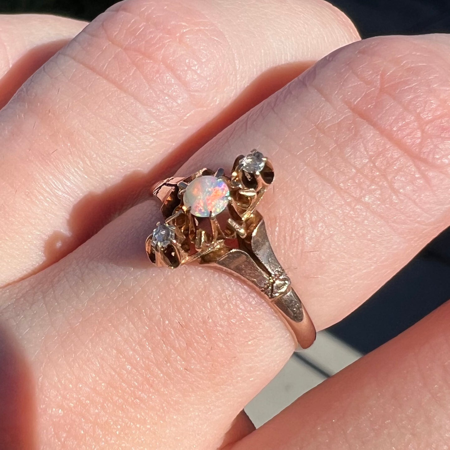 Angled close-up view of an antique gold Victorian opal ring worn on a finger in natural light.  The opal has red play of color.