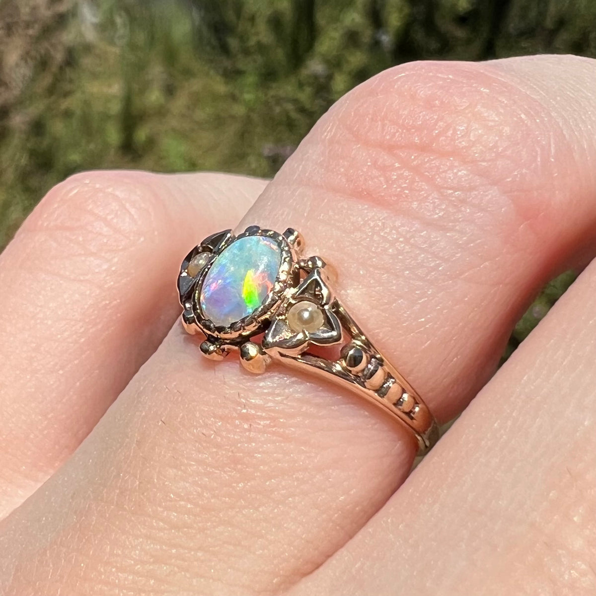 Angled close-up of antique 1890s Victorian opal and seed pearl ring, worn on finger in natural light