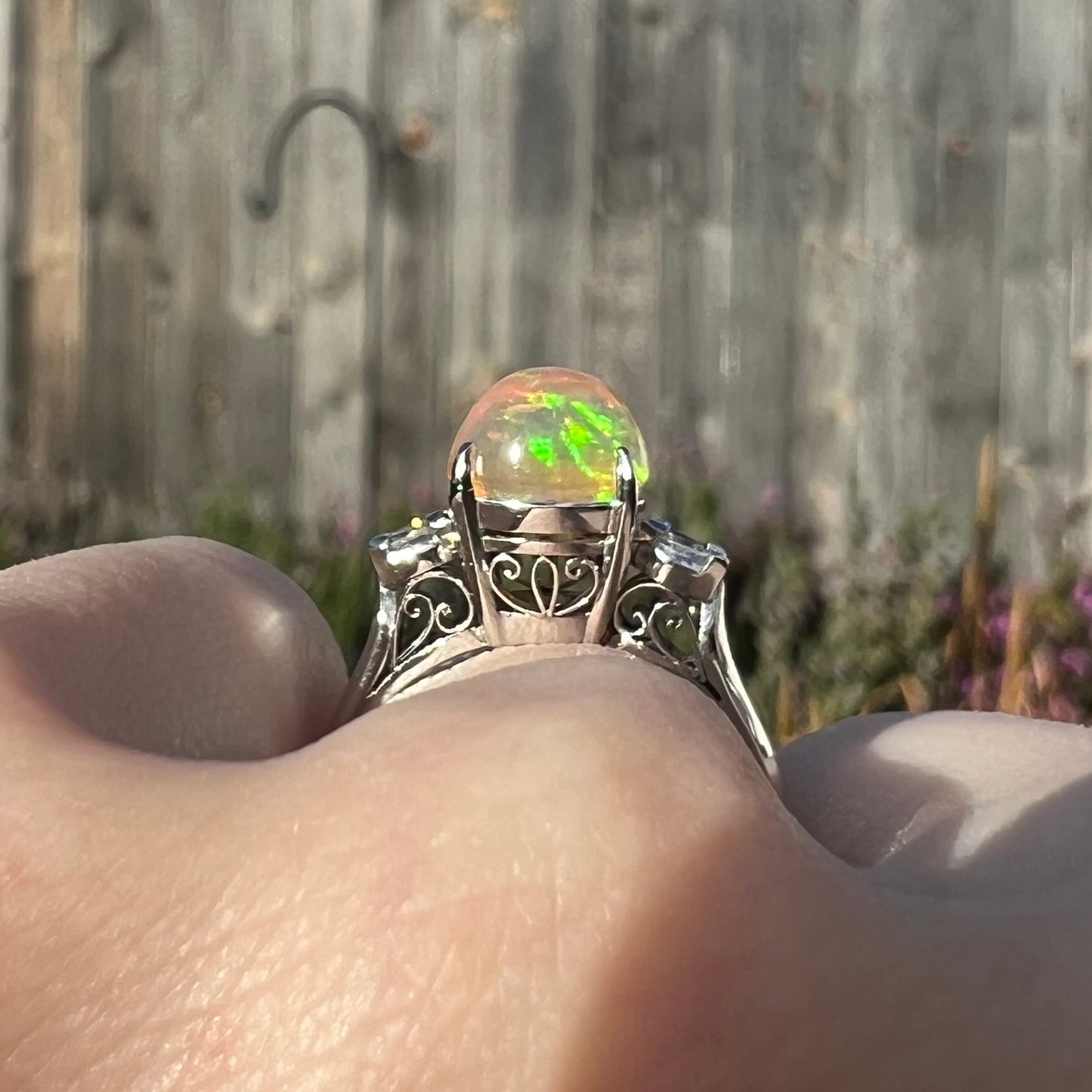 The gallery view of an Art Deco-inspired fire opal and diamond engagement ring in platinum, worn on a hand showcasing filigree designs.