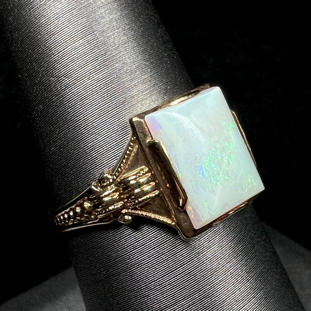 An Art Deco-era 10k gold opal solitaire ring shown close-up from an angle on a ring display