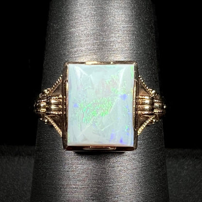 Close-up of a 10k gold Art Deco solitaire ring set with a rectangle cut Australian opal with green and blue flashes of color, shown on ring display