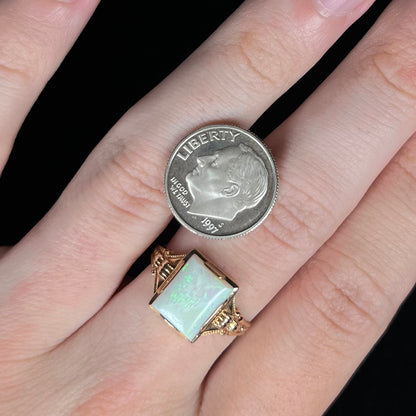 Close-up of hand wearing a gold Art Deco women's ring set with a rectangle cut opal next to a US dime coin for scale