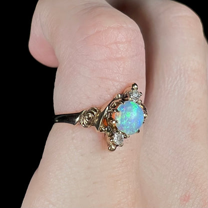 An Art Nouveau era opal and diamond pinky ring made from 10k gold shown close-up from angle on pinky finger