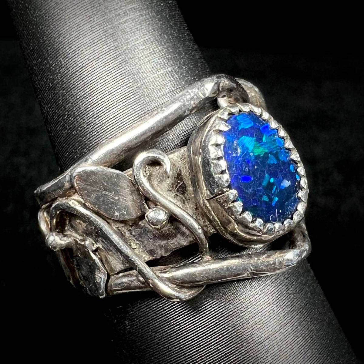 Artisan-made sterling silver black opal doublet ring viewed from angle on ring display, nature-inspired leaf and vine design visible
