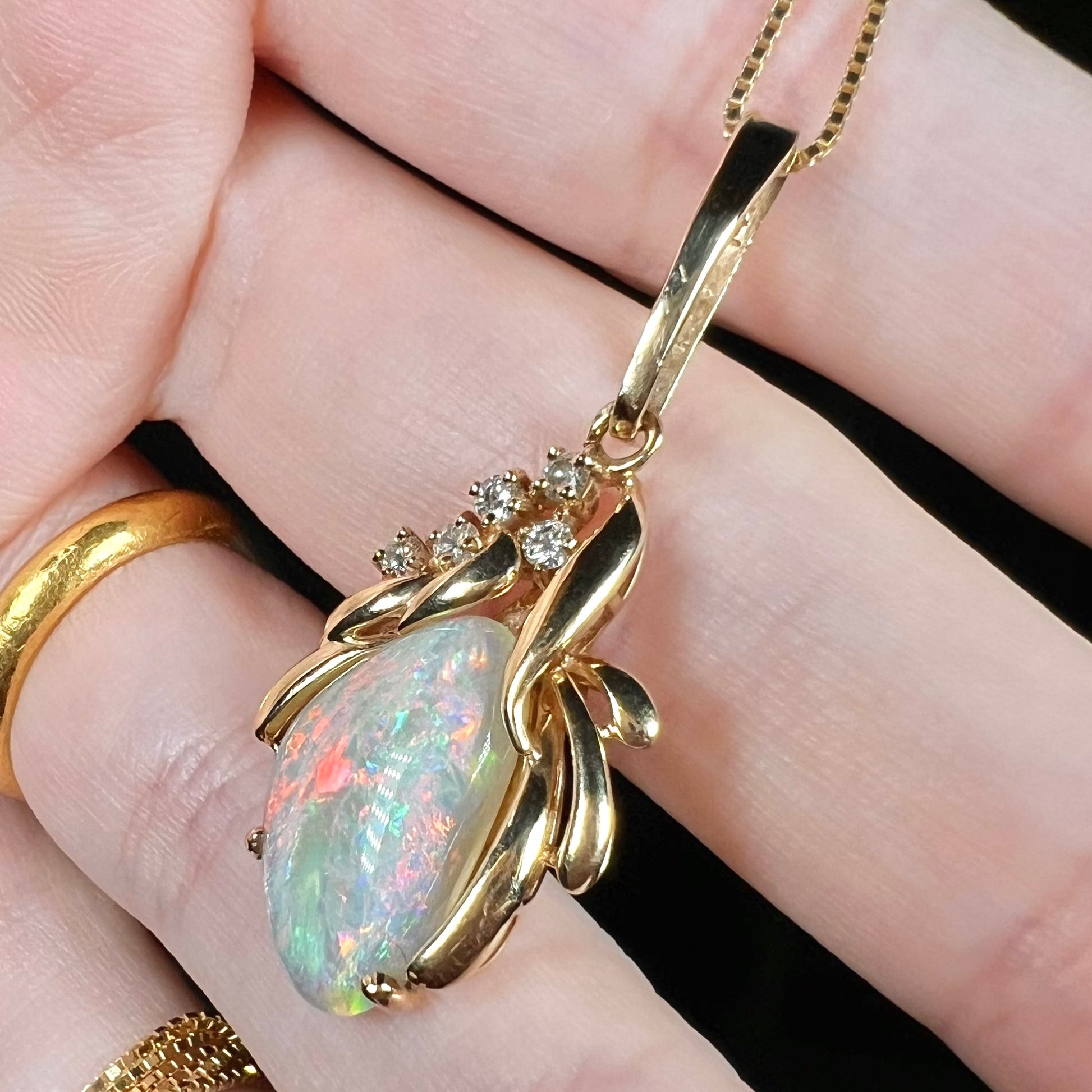 A vintage, women's Australian opal and diamond pendant in 14k gold with an asymmetrical design, shown close-up from an angle in a hand.