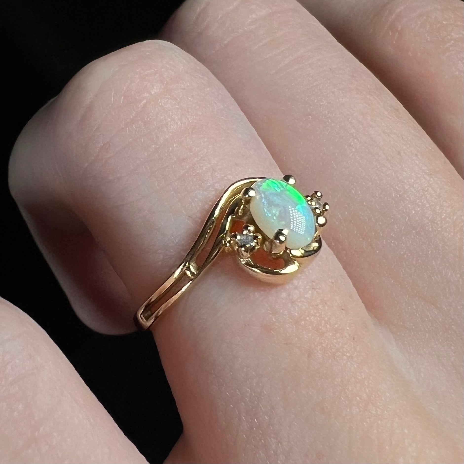 A gold opal ring with an asymmetrical split-shank design worn on a finger, shown from an angled view.