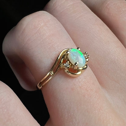 A gold opal ring with an asymmetrical split-shank design worn on a finger, shown from an angled view.