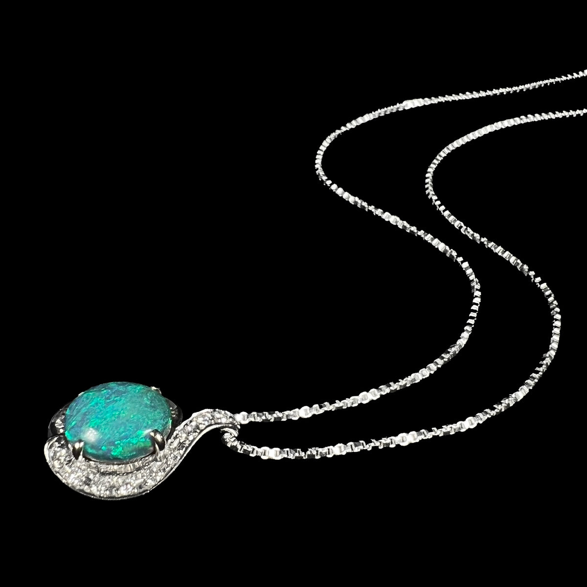 Women's Australian black opal and diamond necklace shown laying on black background, its chain flowing behind the pendant.
