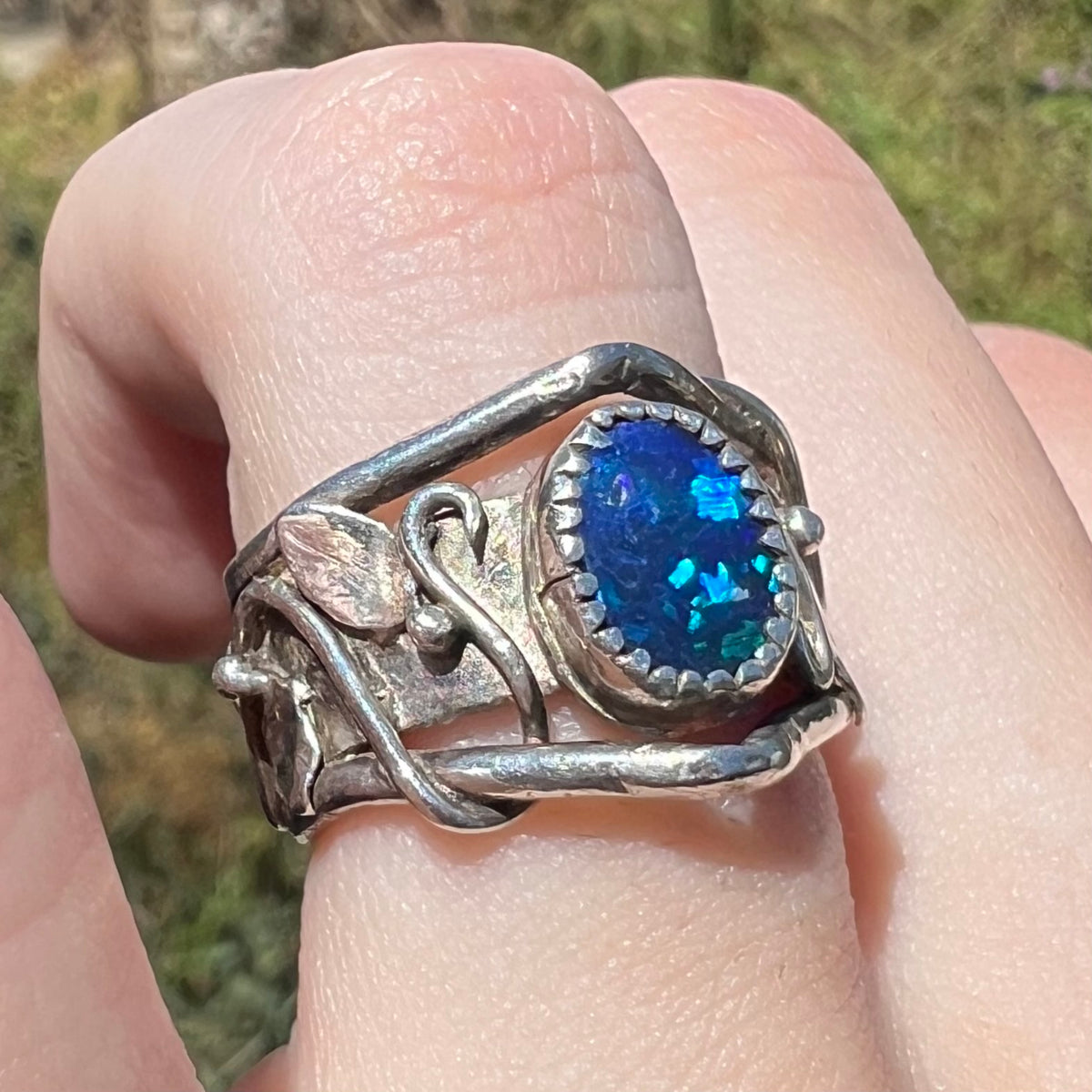 An Australian black opal doublet ring with wide, nature-inspired design, worn on finger and viewed from sunlit angle