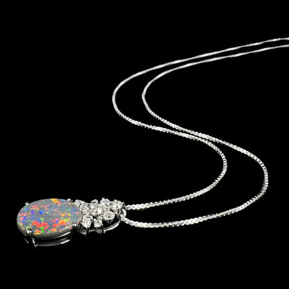 A platinum Australian black opal and diamond necklace with red flashes of play-of-color shown laying on black background, its chain flowing into the distance.