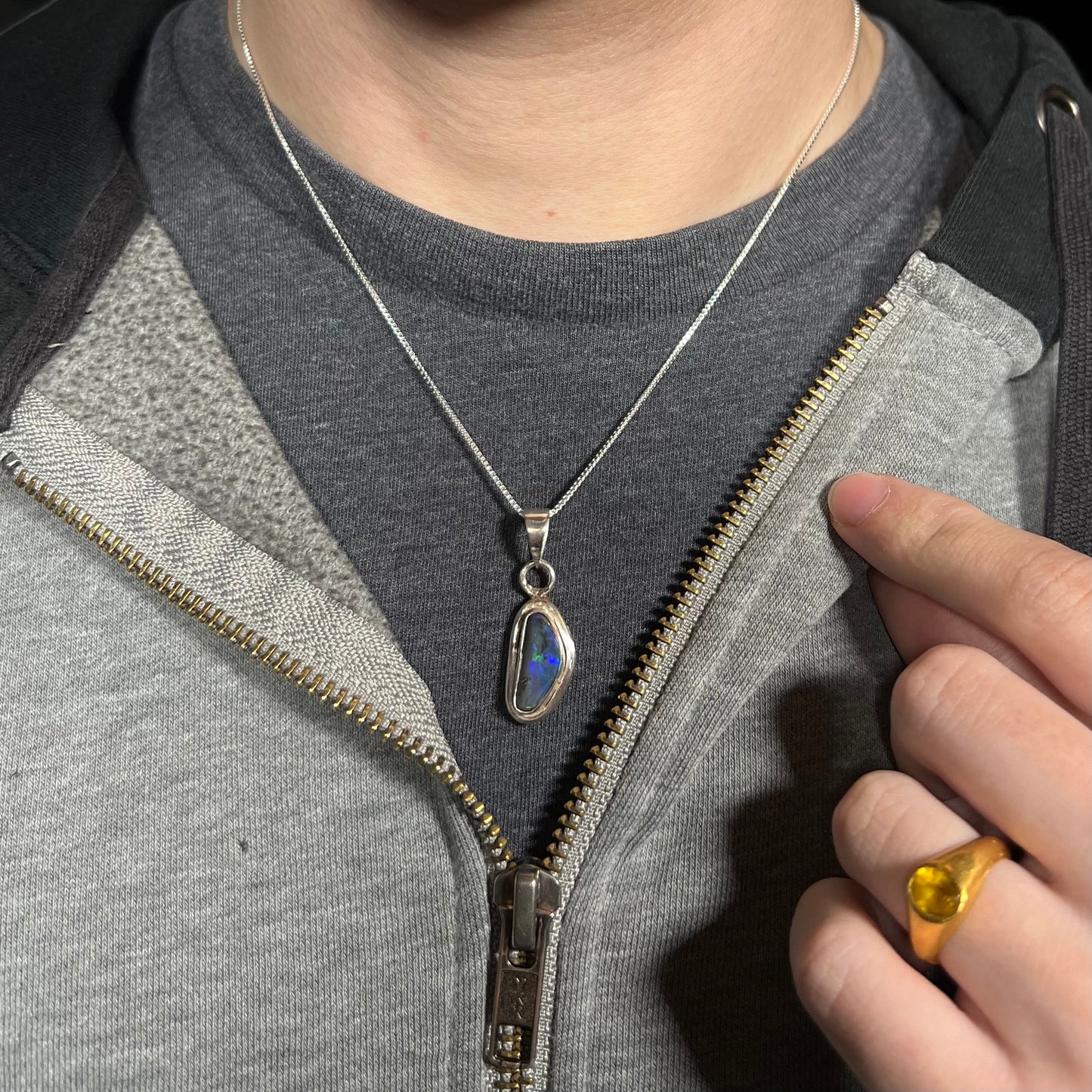 Close-up of person wearing a sterling silver Australian black opal necklace around his neck against a dark shirt beneath a hoodie.