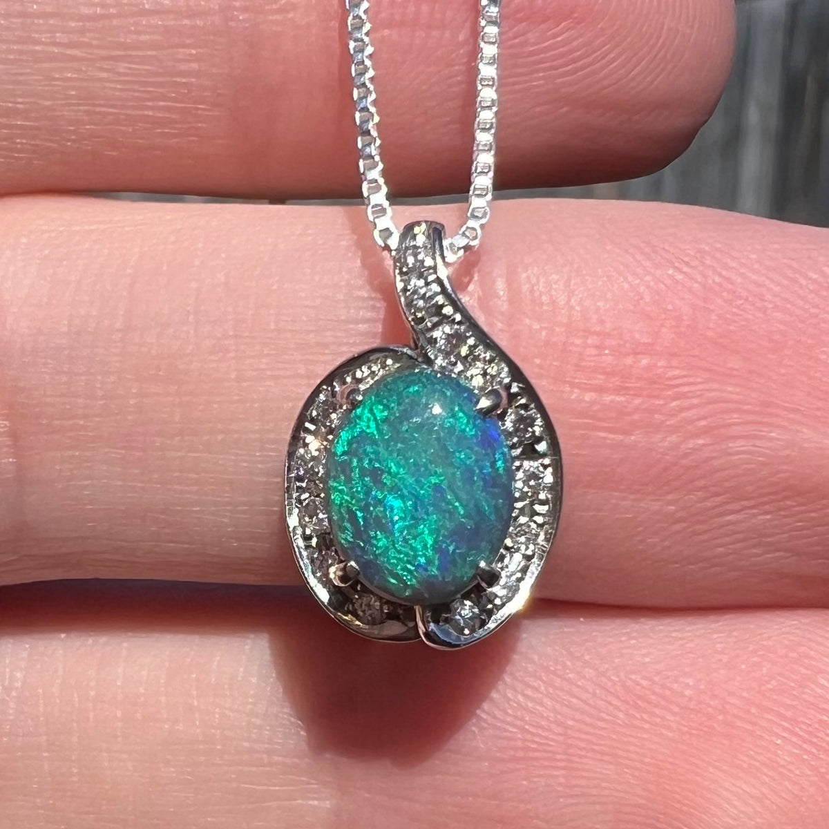 Close-up of Australian black opal pendant with soft blue and green flashes of color, held in hand under natural sunlight.