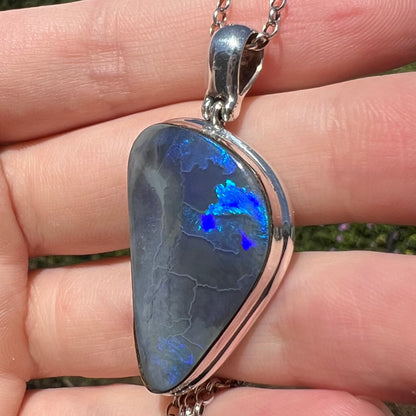 Blue flashes seen in silver Australian black opal pendant viewed close-up from angle, held in hand under sunlight