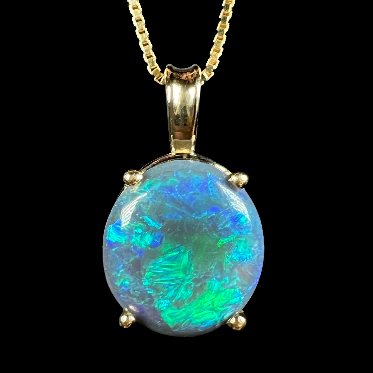 Close-up macro view of Australian black opal pendant in 14k gold with green, blue, and teal flashes of color on chain