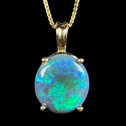 Close-up macro view of Australian black opal pendant in 14k gold with green, blue, and teal flashes of color on chain