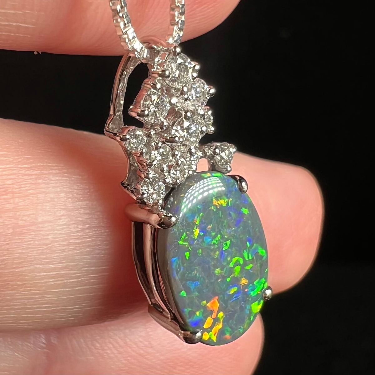 Green, blue, and orange flashes seen in Australian black opal and diamond pendant viewed closely from side angle.