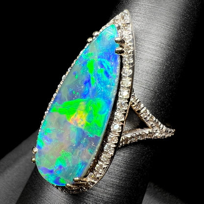 An Australian boulder opal and diamond pave halo engagement ring by OpalPop, shown from an angle on a ring display against a black background.