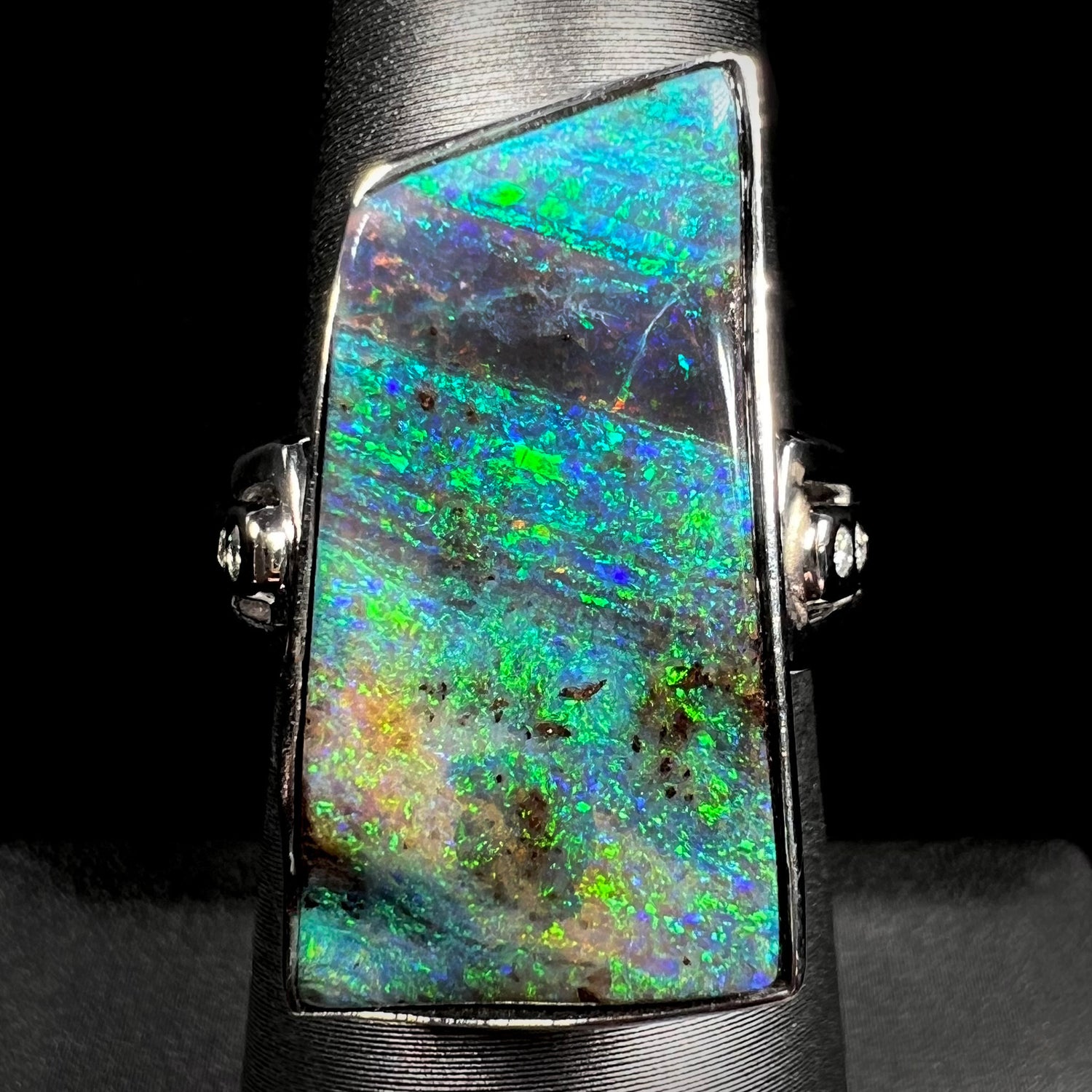 An 11.67ct Australian boulder opal and diamond ring in platinum with green color play, shown on a ring display.