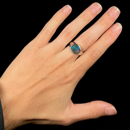 A stainless steel men's Australian boulder opal ring with blue color play, shown on a hand against a black backdrop.