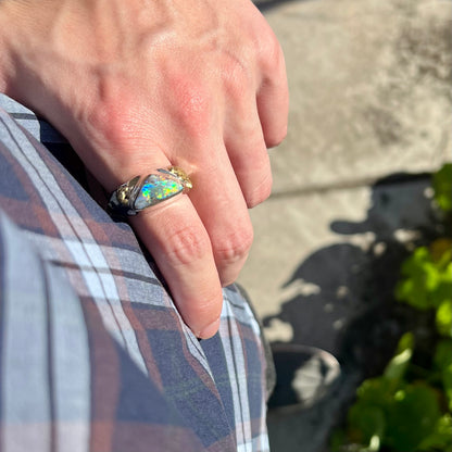 Hand resting on a hip in the sunlight while wearing an Australian boulder opal men's ring.  Blue and green colors can be seen.