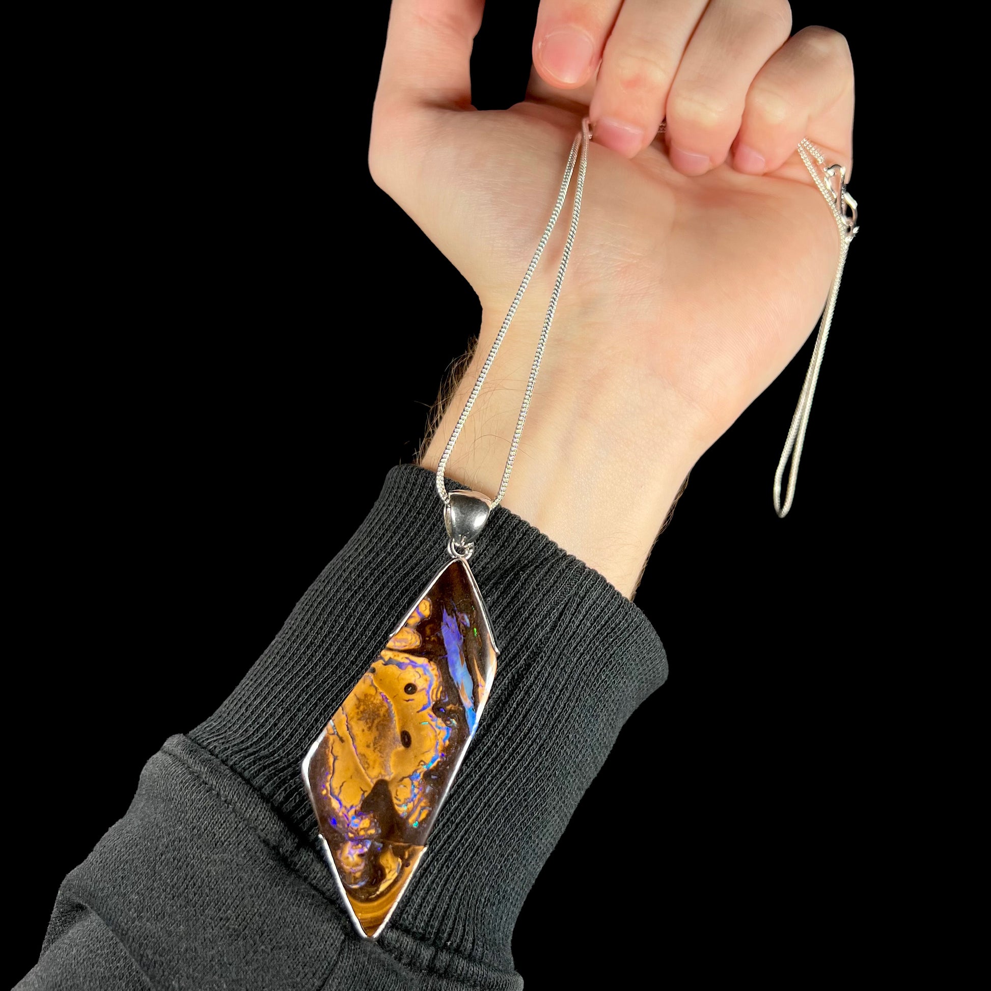 Hand holding large, silver Australian boulder opal statement necklace against wrist