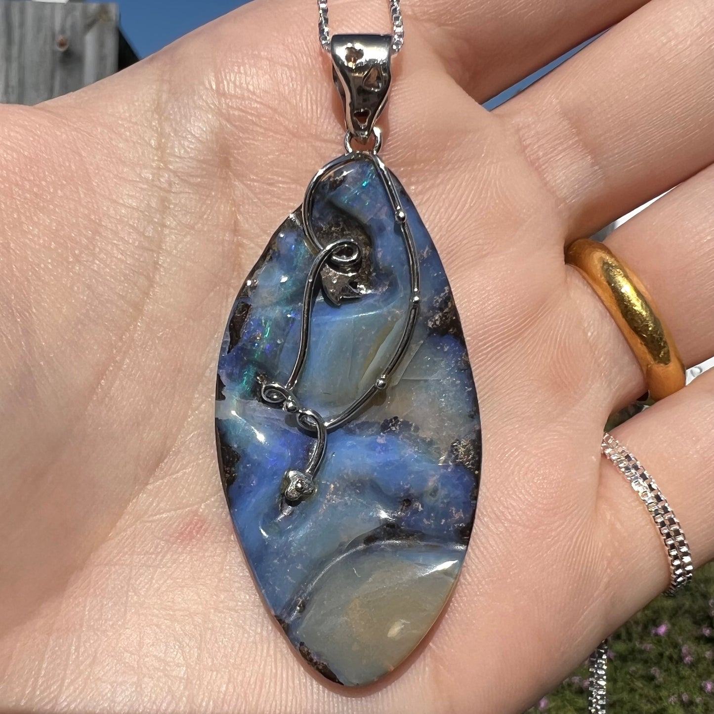 A large, blue Australian boulder opal necklace in sterling silver, shown close-up in a hand in sunlight.
