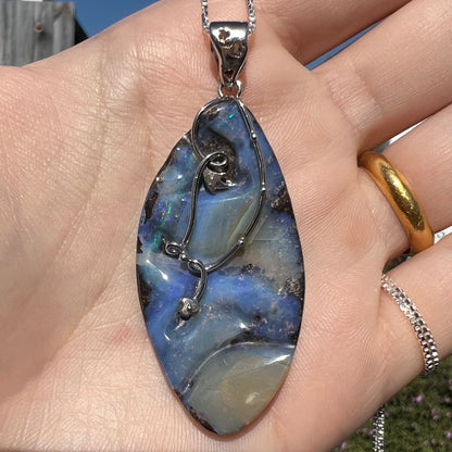 A large, blue Australian boulder opal necklace in sterling silver, shown close-up in a hand in sunlight.