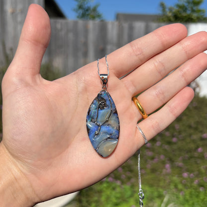 A large, blue Australian boulder opal necklace in sterling silver, shown in a hand in sunlight.
