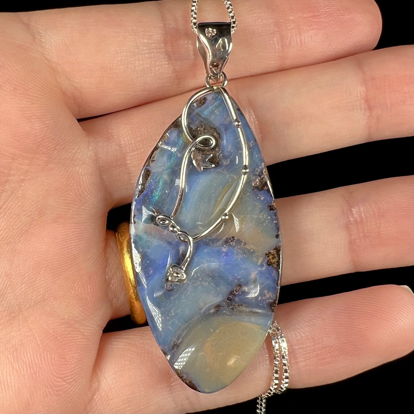 Close-up of a large, blue Australian boulder opal necklace in sterling silver, shown in a hand.