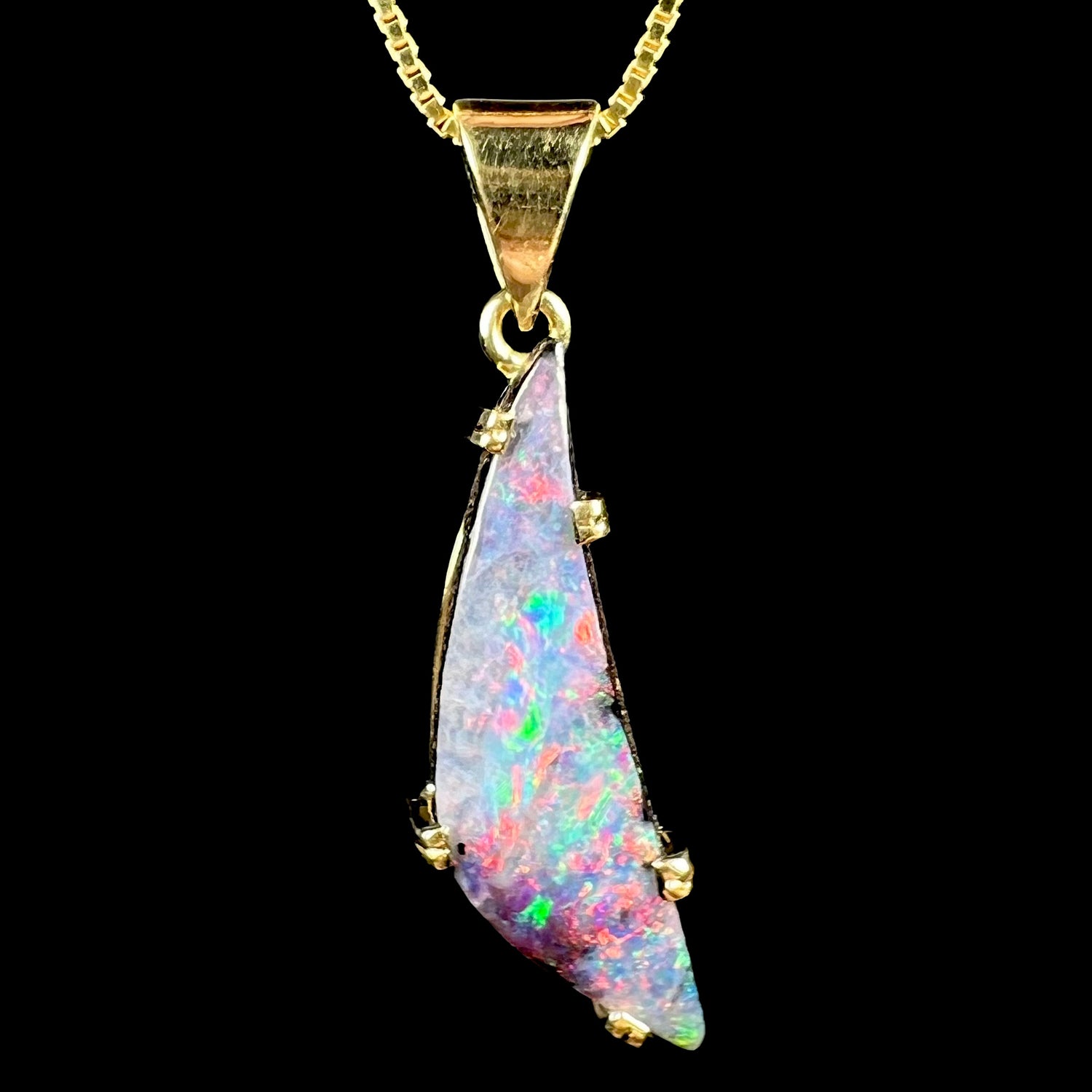 An 18k gold Australian boulder opal pendant with red and green flashes on black background