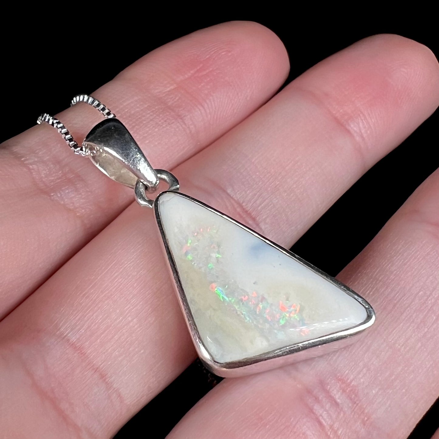 A white Australian boulder opal necklace in .950 silver, shown at an angle close-up in a hand.