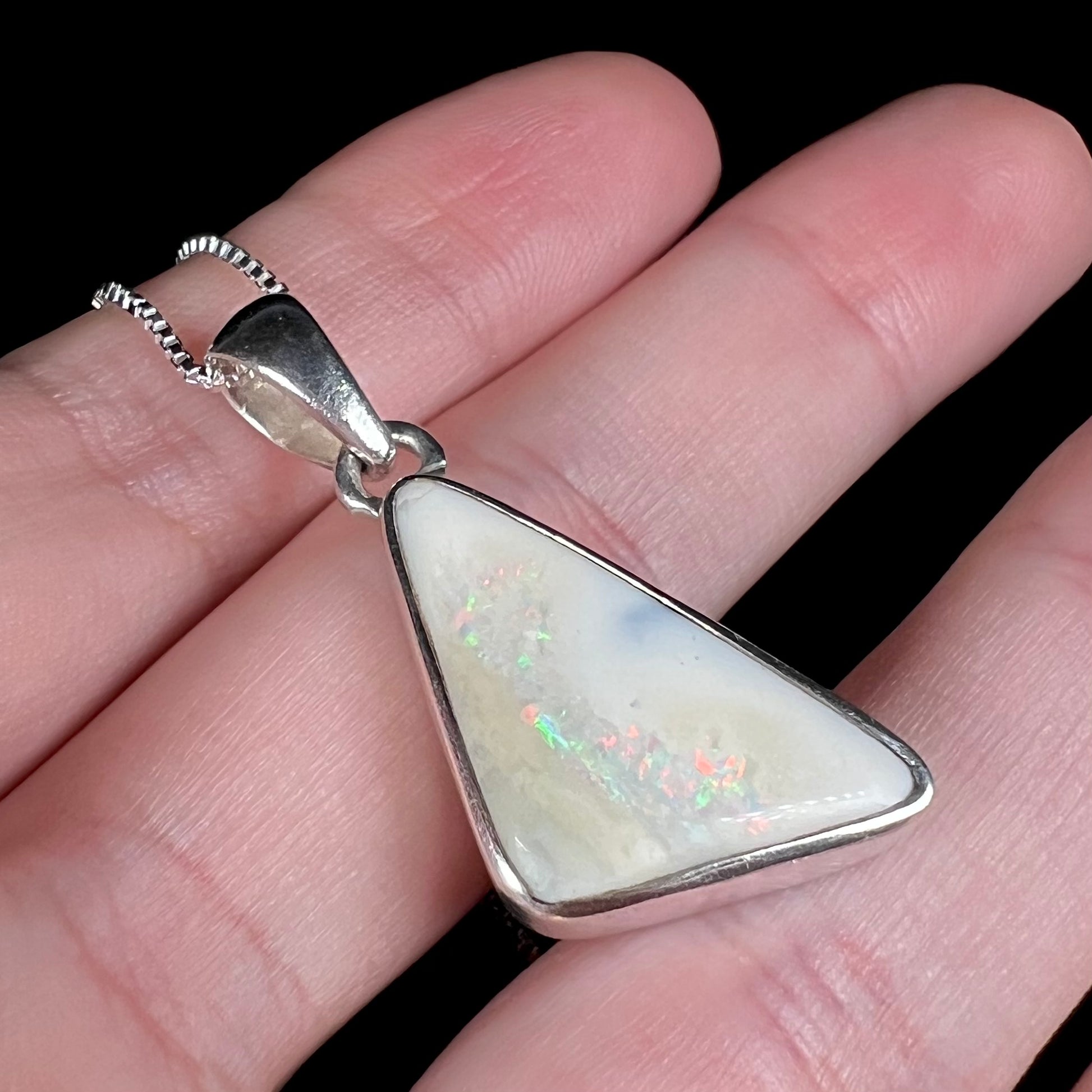A white Australian boulder opal necklace in .950 silver, shown at an angle close-up in a hand.
