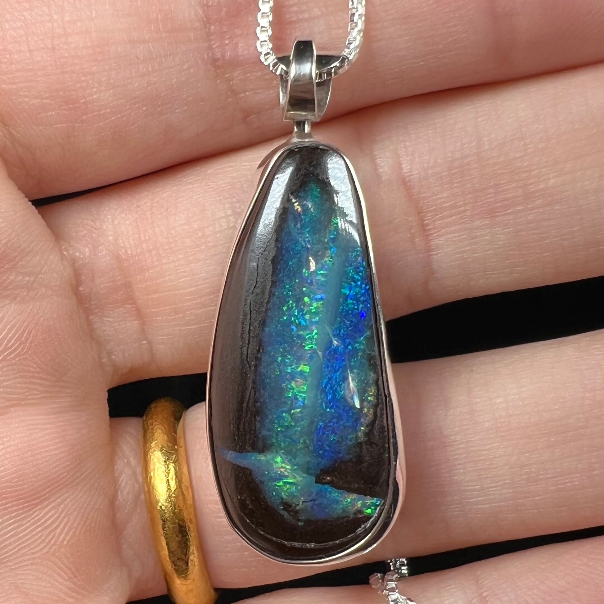Close-up of an Australian boulder opal pendant with glittering blue and green color play, shown in a hand.