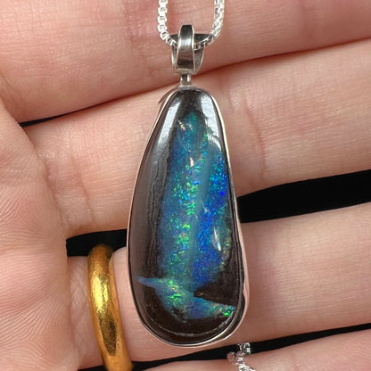 Close-up of an Australian boulder opal pendant with glittering blue and green color play, shown in a hand.