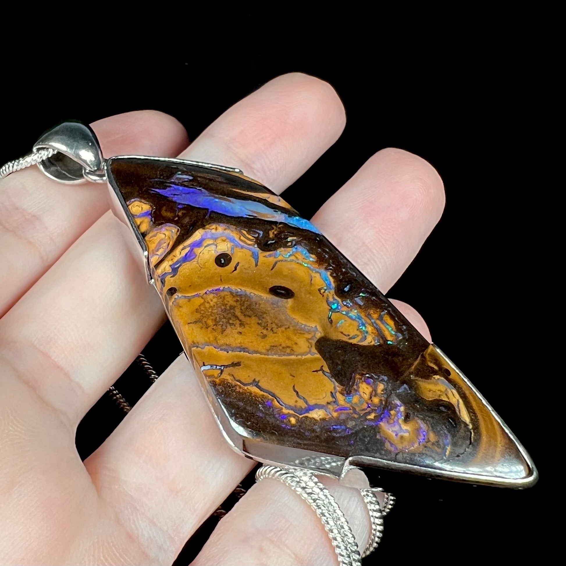 Angled close-up of silver Australian boulder opal pendant with purple and blue colors, held in hand