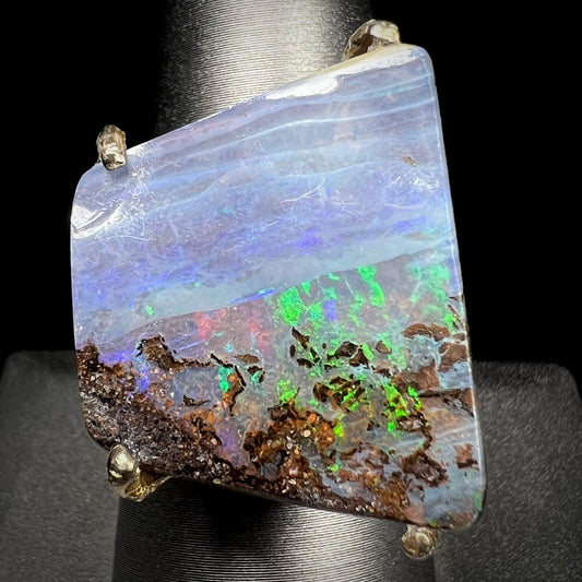 A large Australian boulder opal ring with green flashes, showing the front view against a black background.