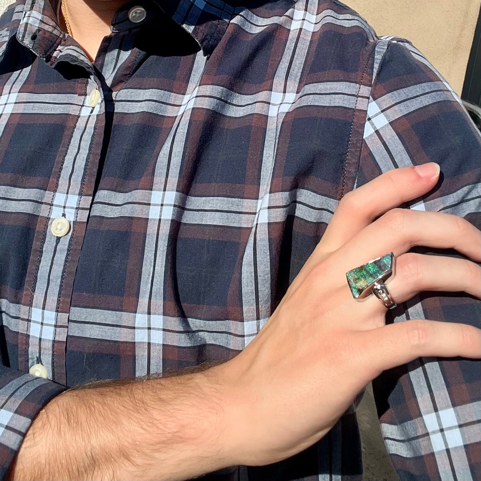 A platinum Australian boulder opal and diamond ring worn on a hand as the hand rests on the model's opposing shoulder.