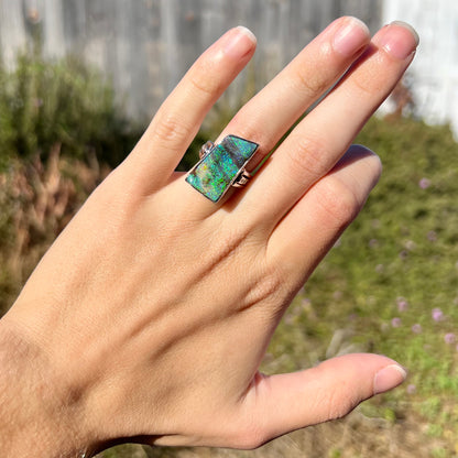 An Australian boulder opal statement ring with green color play in platinum, worn on a hand in sunlight.