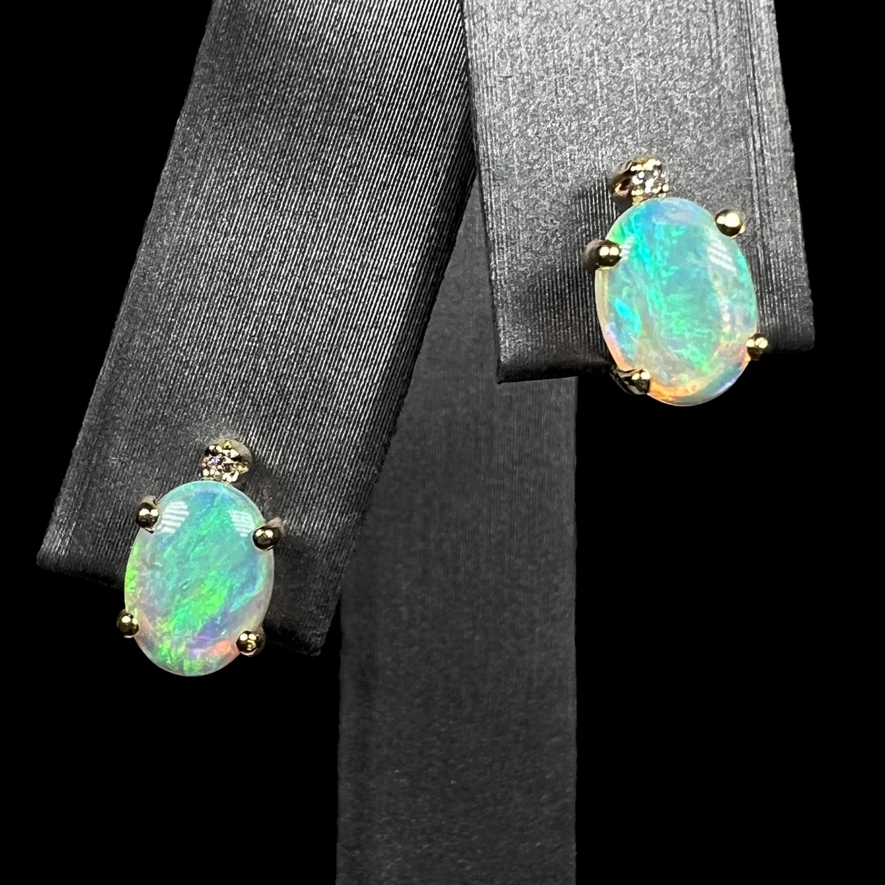A pair of Australian crystal opal and diamond stud earrings in gold with green-blue color play shown on an earring display.