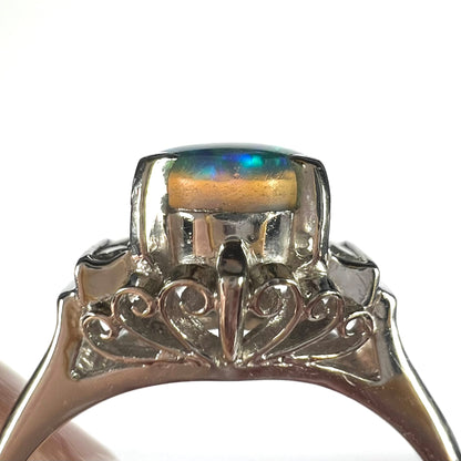 Side gallery view of natural Australian black opal ring showing translucent crystal opal above naturally occuring seam of black potch matrix, shown against white background.