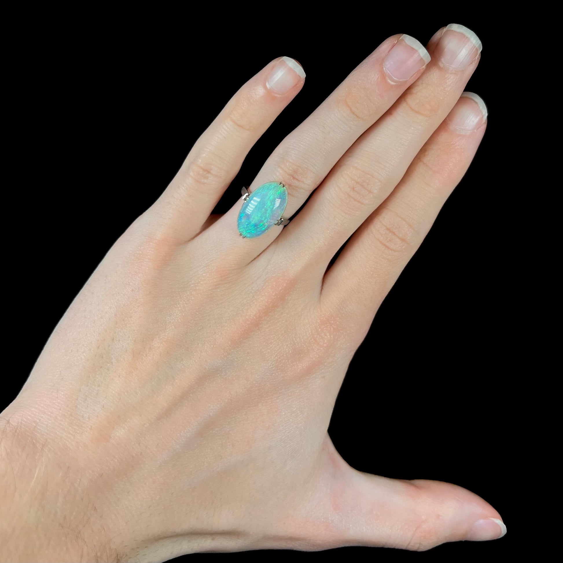 An Australian crystal opal solitaire ring, cast in platinum, worn on a hand.