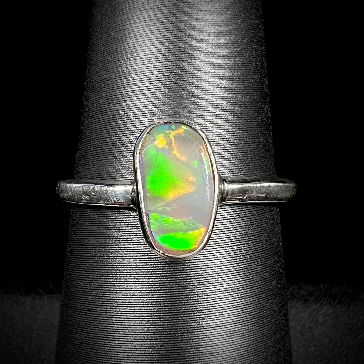 Green flashes are seen in the front view of a silver Australian crystal opal solitaire ring.  The ring sits on a ring display.
