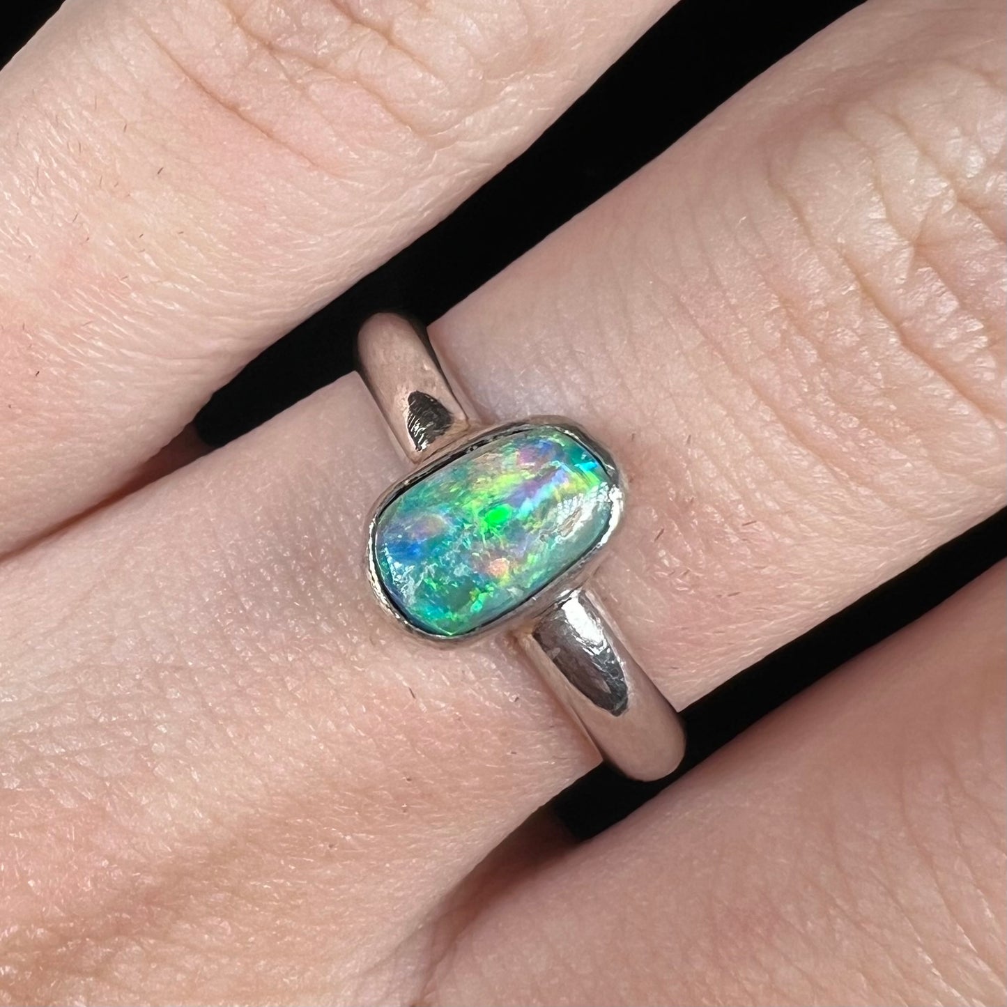 Close-up of silver Australian crystal opal solitaire ring worn on finger